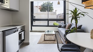 A modern kitchen with a built-in oven and microwave, a dining area with a round table and a sofa, and a large window offering a city view. - Valencia Apartments by Olala Homes (València)