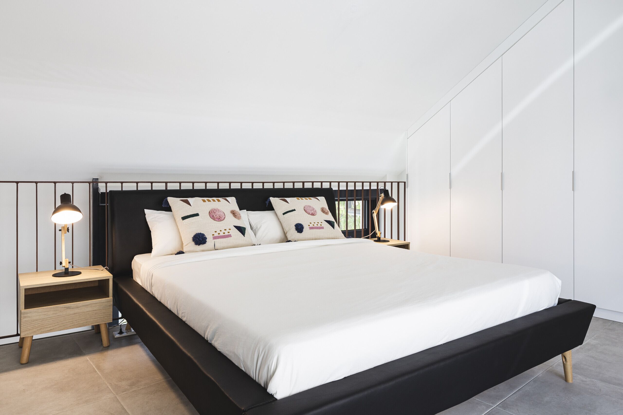 Un dormitorio moderno con una cama de estructura negra, ropa de cama blanca y dos lámparas de noche.
