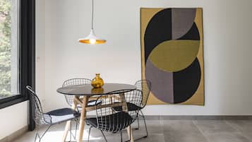 Un comedor con una mesa redonda, sillas negras de estructura de alambre, un florero amarillo y una lámpara colgante.