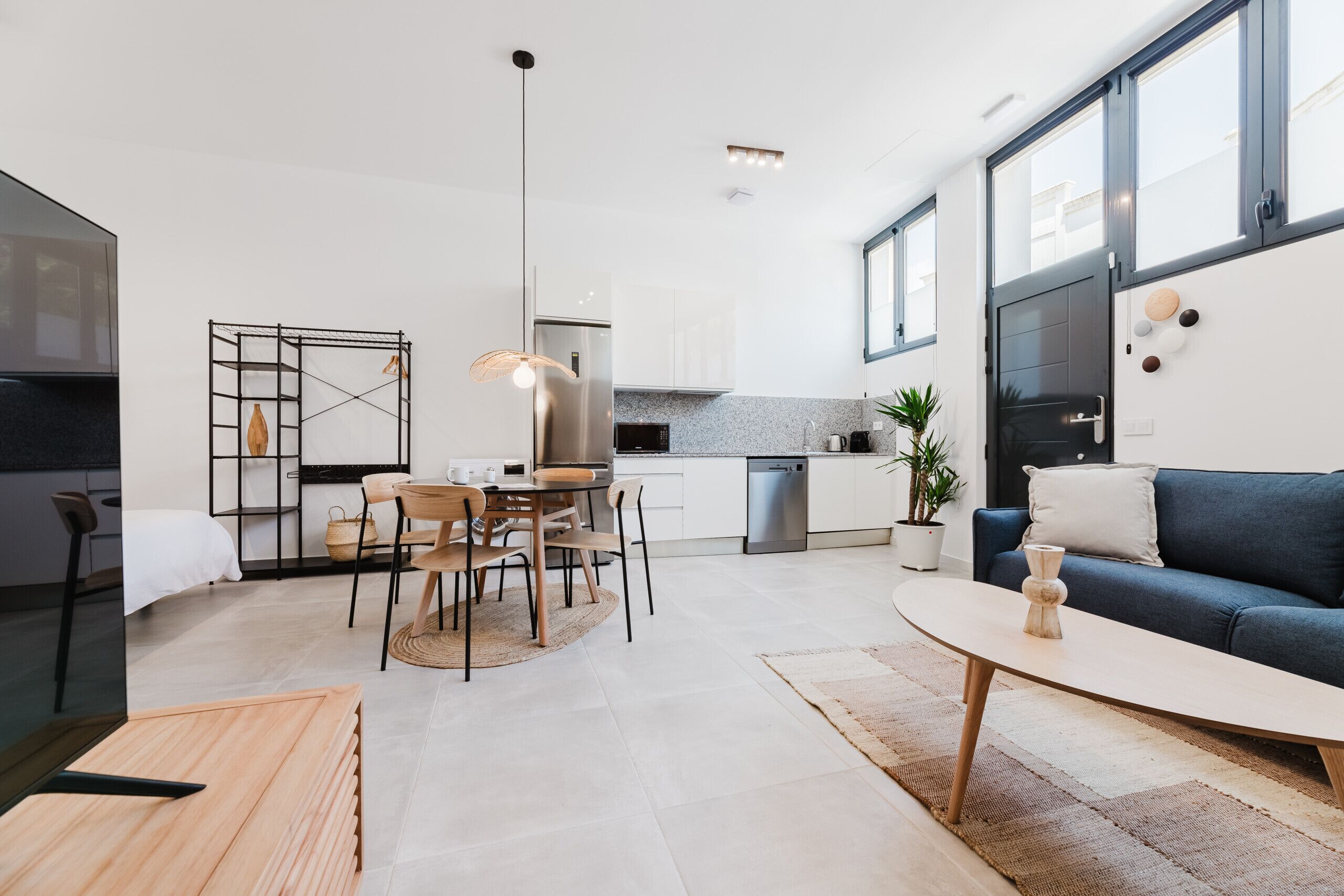 A modern kitchen with white cabinets, a stainless steel refrigerator, and a dining area with a table and chairs.