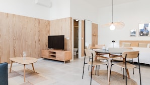 A modern hotel room with a wooden accent wall, a flat-screen TV, a dining area with a table and chairs, and a bed with a headboard. - Valencia Apartments by Olala Homes (València)