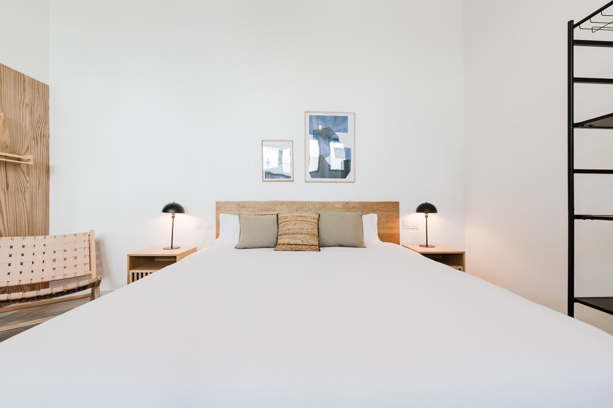 Un dormitorio ordenado con una cama grande, dos mesitas de noche con lámparas, un cabecero de madera y dos cuadros enmarcados en la pared.