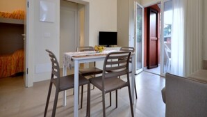 A dining area with a table, chairs, and a television. There is a bed with a patterned blanket in the background. - Completely renewed house in Bibione (Bibione)