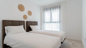 Een hotelkamer met twee bedden, een groot raam met dunne gordijnen en drie geweven wanddecoraties.