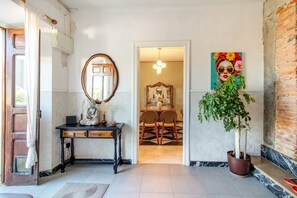 A hallway with a wooden door, a mirror, a desk with drawers, a dining area with chairs and a table, and a potted plant. - Villa Vista Ajo – 17th-Century Manor with Views, Garden, and Beach Nearby (Bareyo)