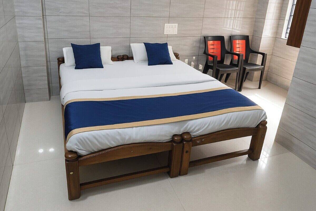 A neatly made bed with a blue and white bedspread, wooden headboard, and two bedside tables with red chairs.