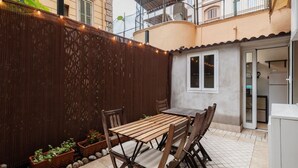 Une terrasse avec une table et des chaises en bois, une clôture en métal ondulé et des plantes en pot.