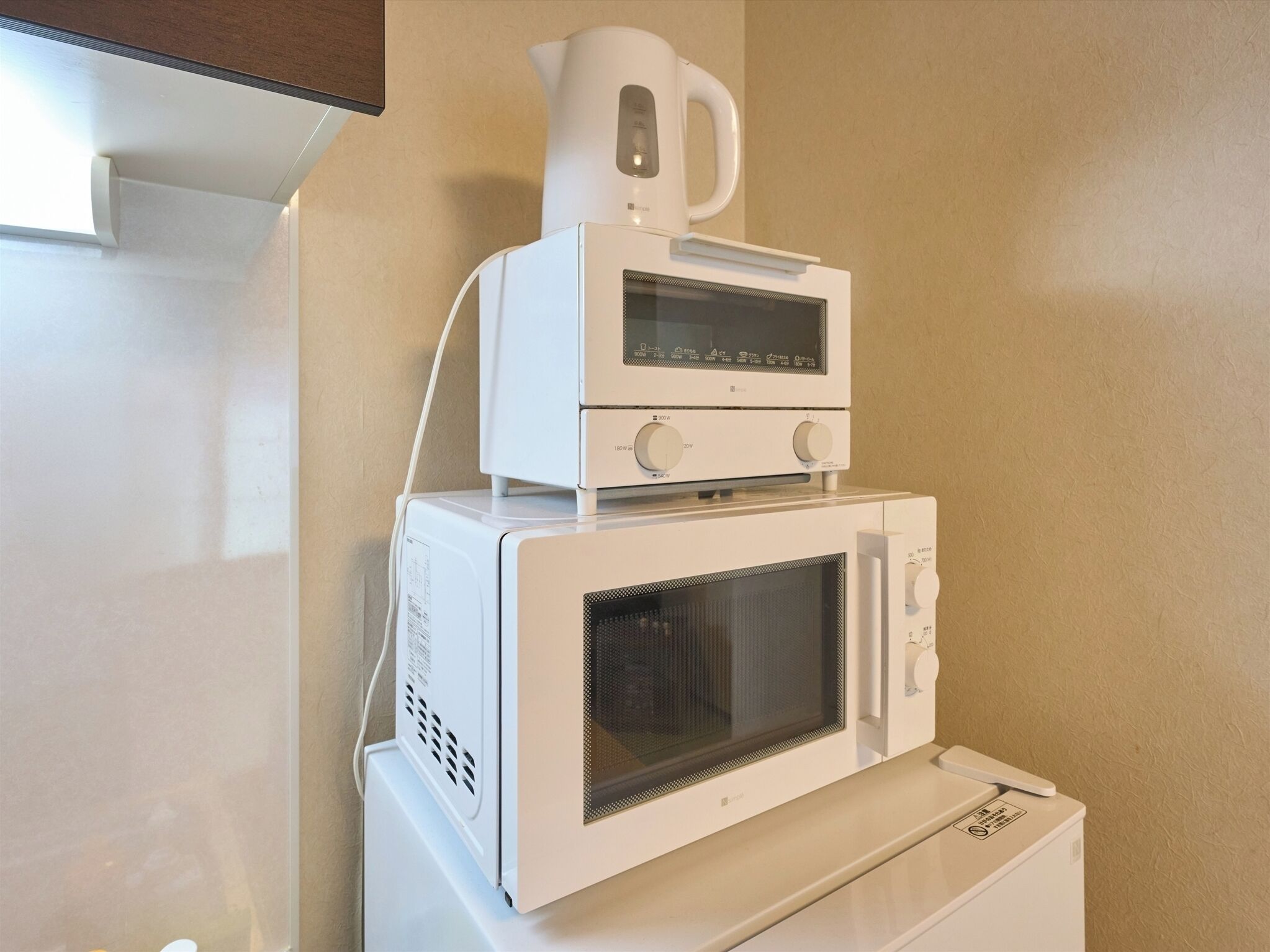 A compact microwave oven with a kettle on top, placed on a white appliance.
