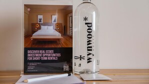 Un folleto sobre oportunidades de inversión inmobiliaria con una botella etiquetada 'POUMAX' y un bolígrafo sobre una mesa.