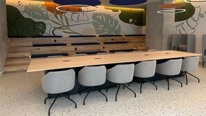 Ein Konferenzraum mit einem langen Tisch, sechs grauen Stühlen und einer Wandmalerei mit abstrakten Pflanzenmotiven.
