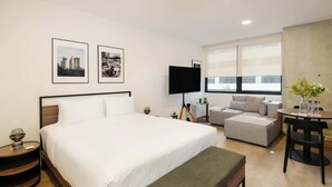 Ein modernes Hotelzimmer mit einem großen Bett, einer Couch, einem kleinen Tisch mit Blumen und einem Fernseher.