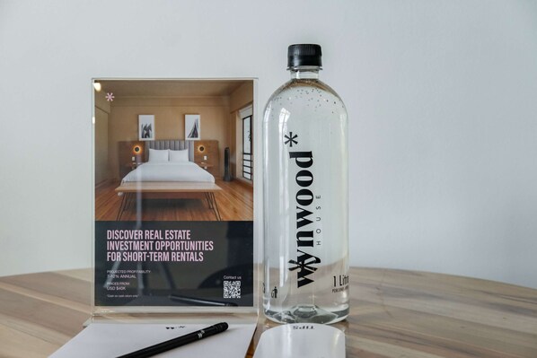Un folleto sobre una oportunidad de inversión inmobiliaria, una botella con la etiqueta 'POWAX HOUSE' y un bolígrafo sobre una mesa.