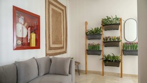 A living room with a grey sofa, a red-framed picture, a large woven rug, and a wall-mounted plant shelf. - w Ravishing 2BR in the Heart of Bocagrande (Cartagena)