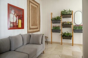 A living room with a grey sofa, a red-framed picture, a large woven rug, and a wall-mounted plant shelf. - w Ravishing 2BR in the Heart of Bocagrande (Cartagena)