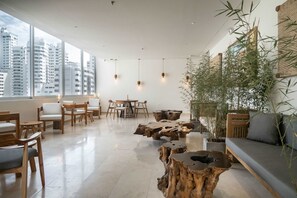 Un salon moderne avec un plafond haut, de grandes fenêtres et une vue sur les immeubles de la ville. On y trouve des chaises en bois, une table ronde et un canapé.