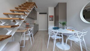 A modern kitchen with a wooden staircase, white chairs, and a dining table. - Luminous duplex in Fuente del Berro (Madrid)