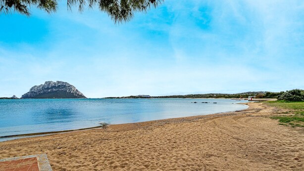 A beach with a rocky outcrop in the distance, a sandy shore, and a clear sky. - Holiday Home 'Porto San Paolo A 50 Mt Dal Mare' with Private Terrace, Wi-Fi and Air Conditioning (Porto San Paolo)
