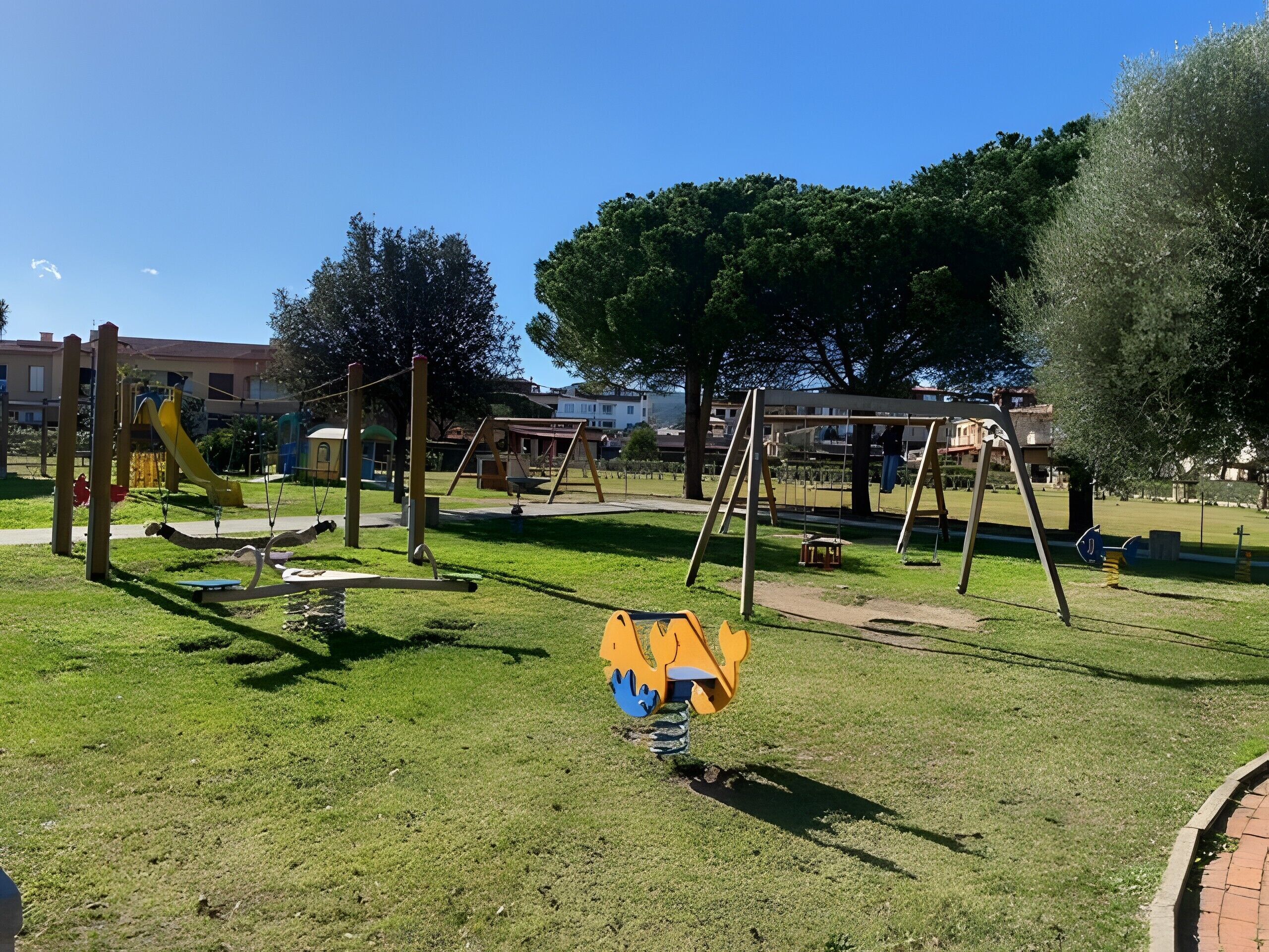 A playground with swings and slides, surrounded by grass and trees.