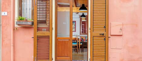 A building with a wooden door, a window with a plant, and a light fixture.