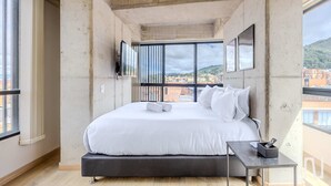 Ein modernes Schlafzimmer mit einem großen Bett, einem kleinen Nachttisch und einem an der Wand befestigten Fernseher.