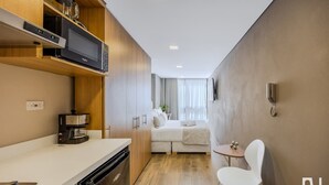 Une chambre d’hôtel compacte comprenant un coin cuisine, un lit, une petite table et une chaise.