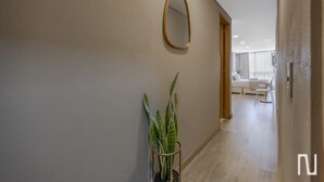 Un couloir avec une plante en pot, un miroir et une vue sur un espace de vie comprenant un canapé et une table à manger.