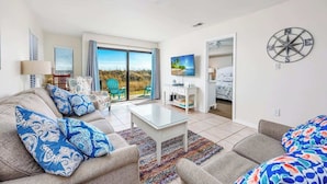 A spacious living room with a large sofa, a coffee table, and a view of the outdoors through a sliding glass door. - Spacious Beachfront 3br, 2ba Condo in Cherry Grove (Myrtle Beach)
