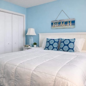 Ein Schlafzimmer mit einem weißen Bett, blauen Wänden und einem Schild mit der Aufschrift 'BEACH'.