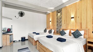 Une chambre moderne avec deux lits, une petite kitchenette et un mur d’accent en pierre.