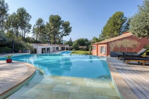 A swimming pool with a wooden deck, lounge chairs, and a building with a red facade. - La Maison Du Castellet (Le Castellet)