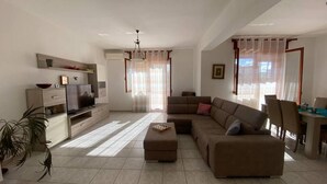A modern living room with a sectional sofa, a TV, and a dining area with a table and chairs. - AffittaSardegna - Casa Turris (Porto Torres)