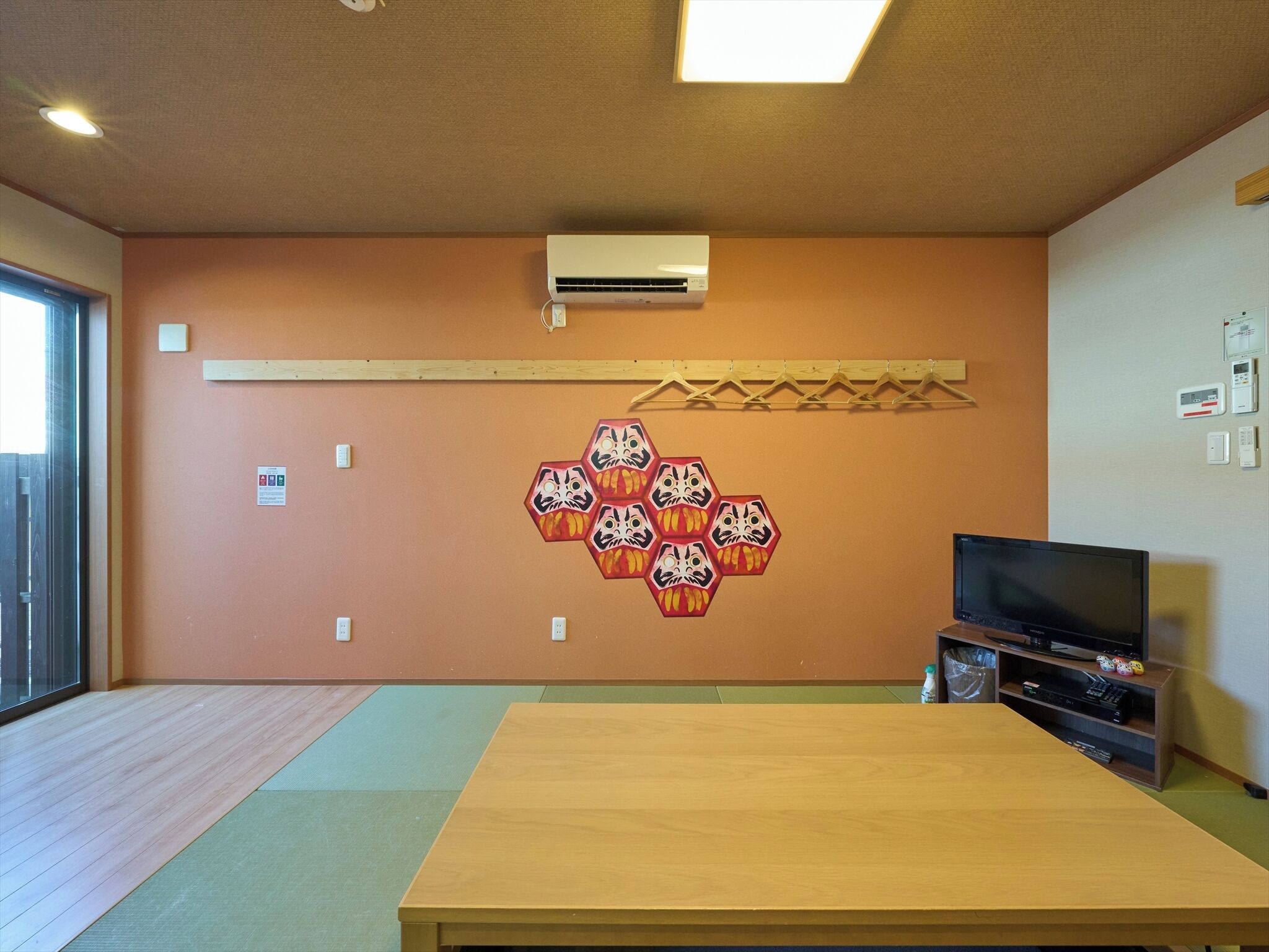 Um quarto com uma mesa de madeira, uma televisão e um ar condicionado fixado na parede.