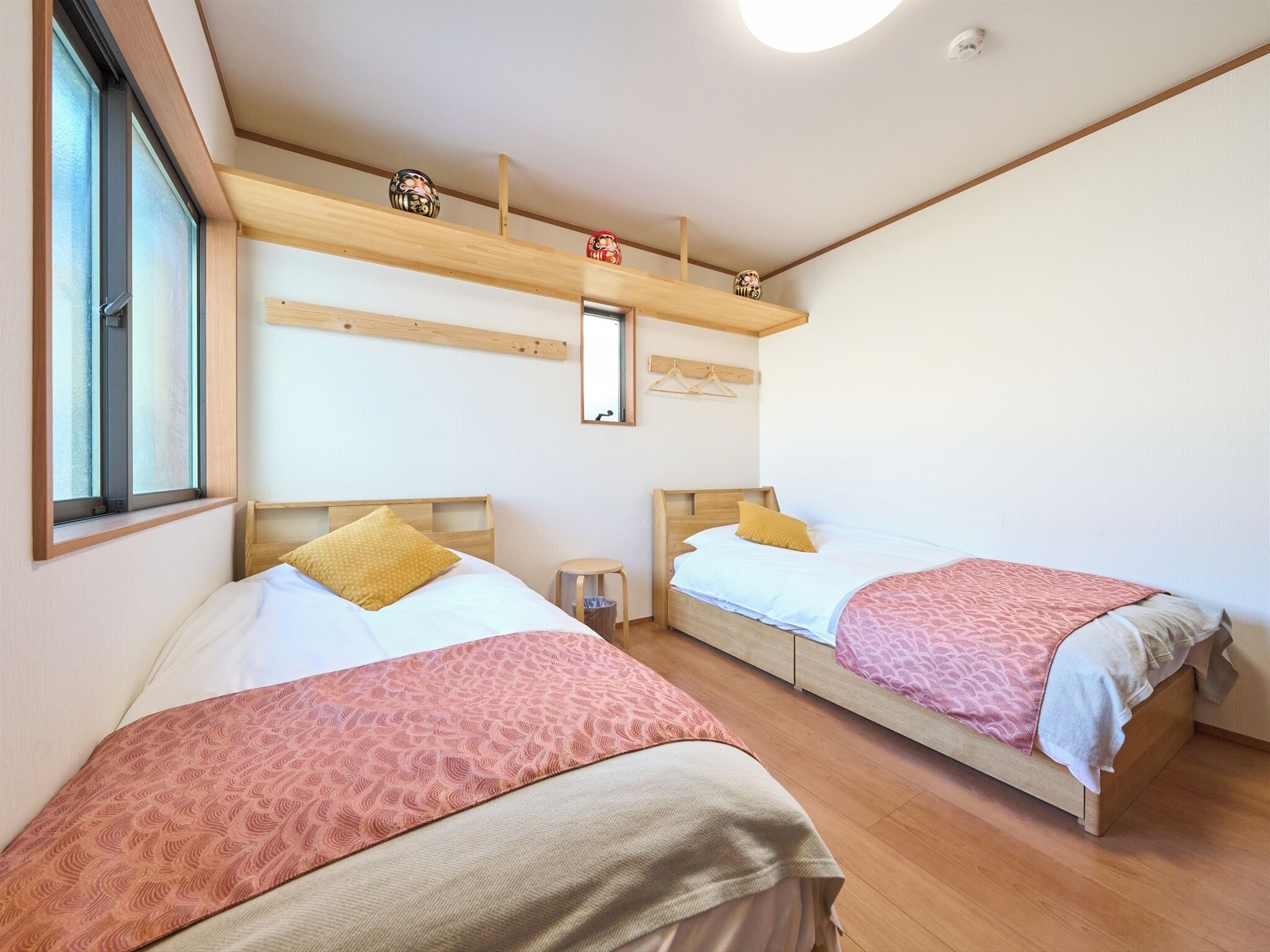 A room with two beds, wooden headboards, a small stool, a mirror, and a shelf with decorative items.