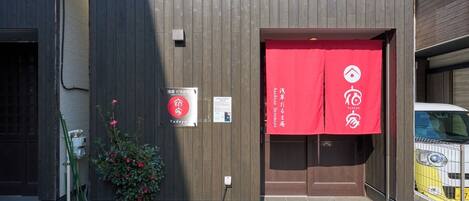 A building with a wooden facade, a red entrance banner, and a small sign with Japanese text.