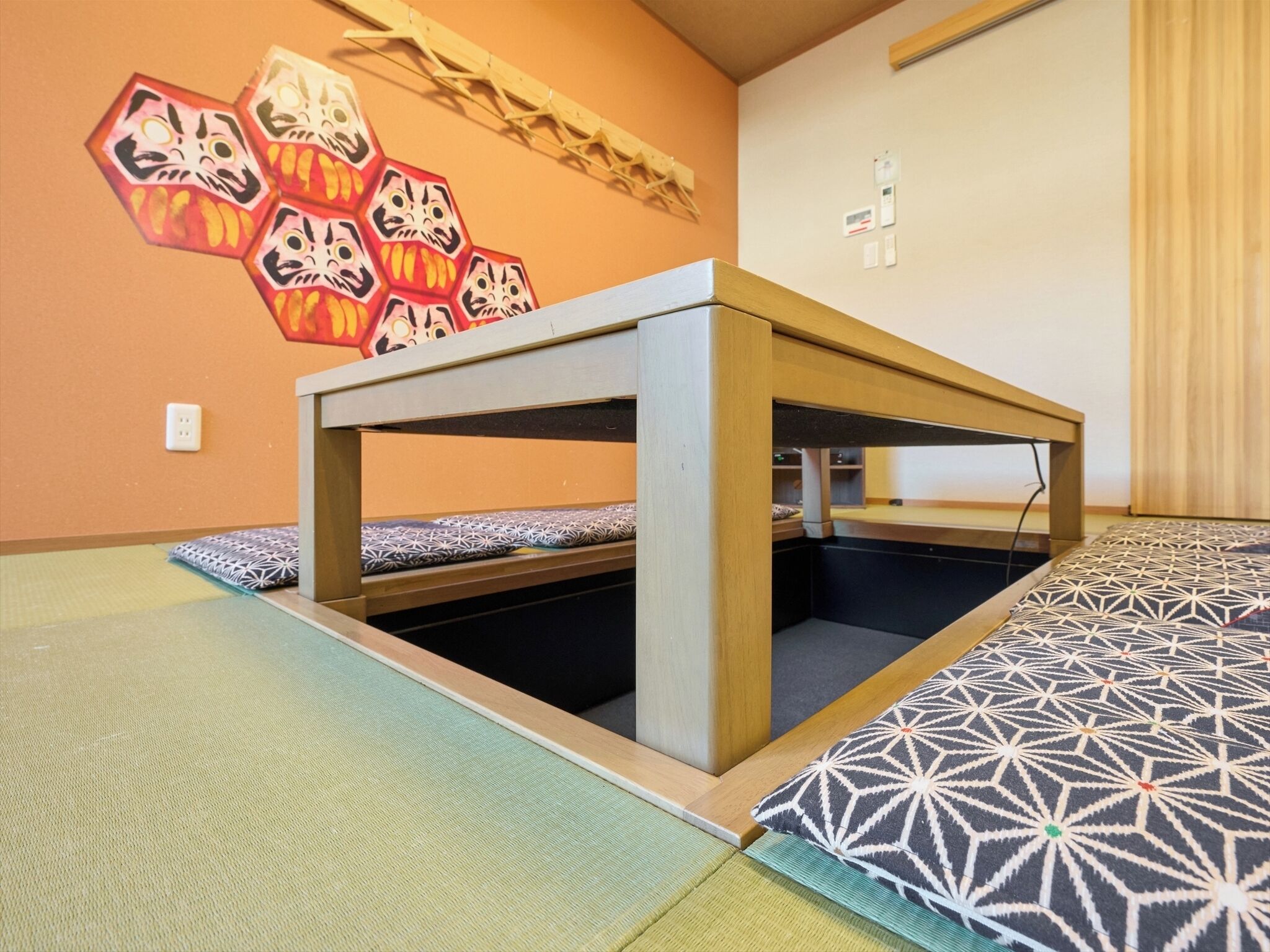 A room with a low wooden bed, a small table, and a wall decorated with hexagonal patterns.