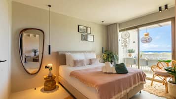 A bedroom with a bed, a mirror, a bedside table with a vase, a balcony with chairs and a table, and framed pictures on the wall.