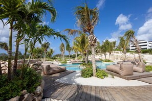 A poolside area with wooden decking, lounge chairs, and palm trees. - The Reef Superior Penthouse With Ocean View (Sint Michiel)