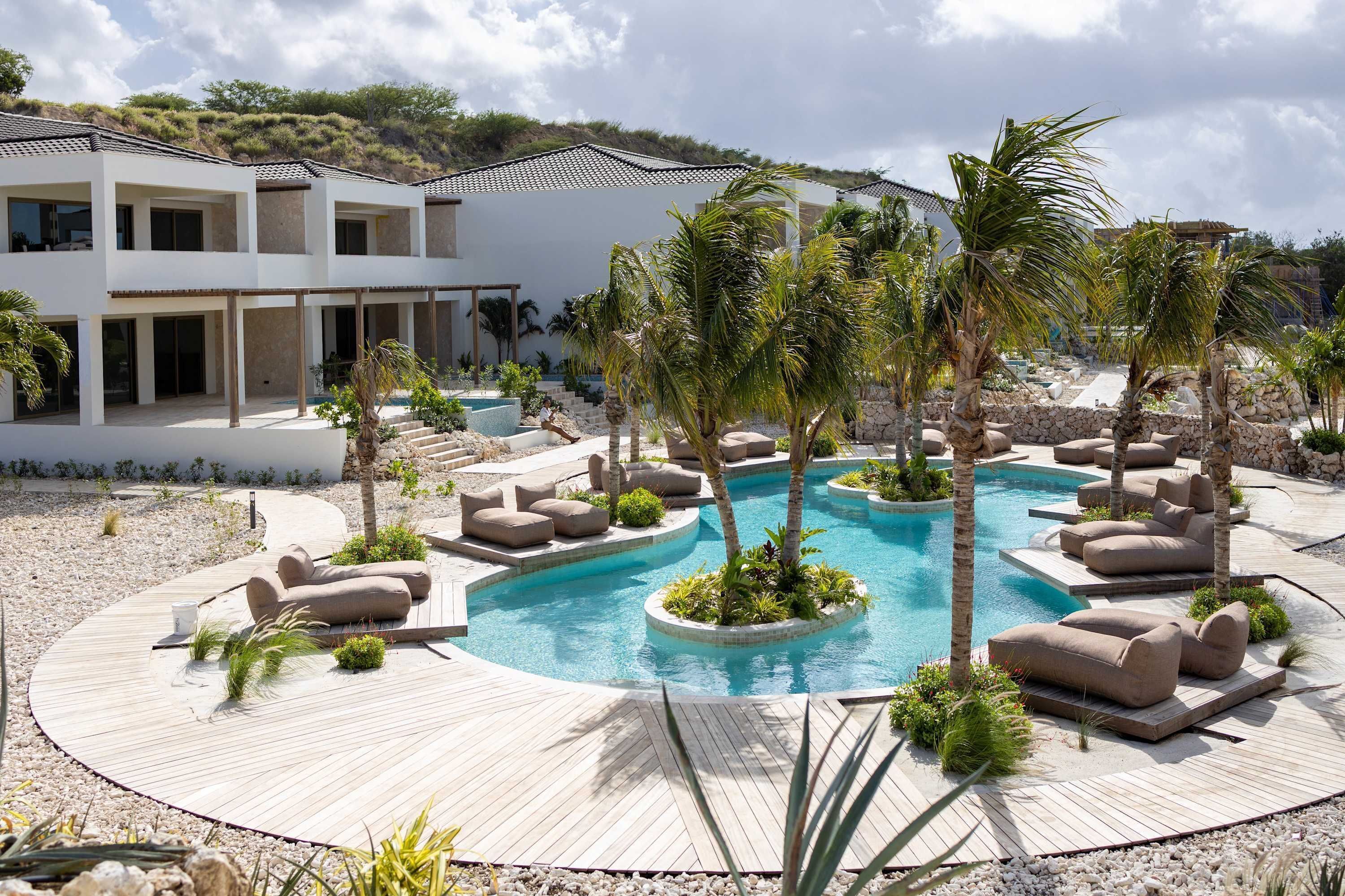 A modern resort with a central pool, outdoor seating, and a multi-story building.