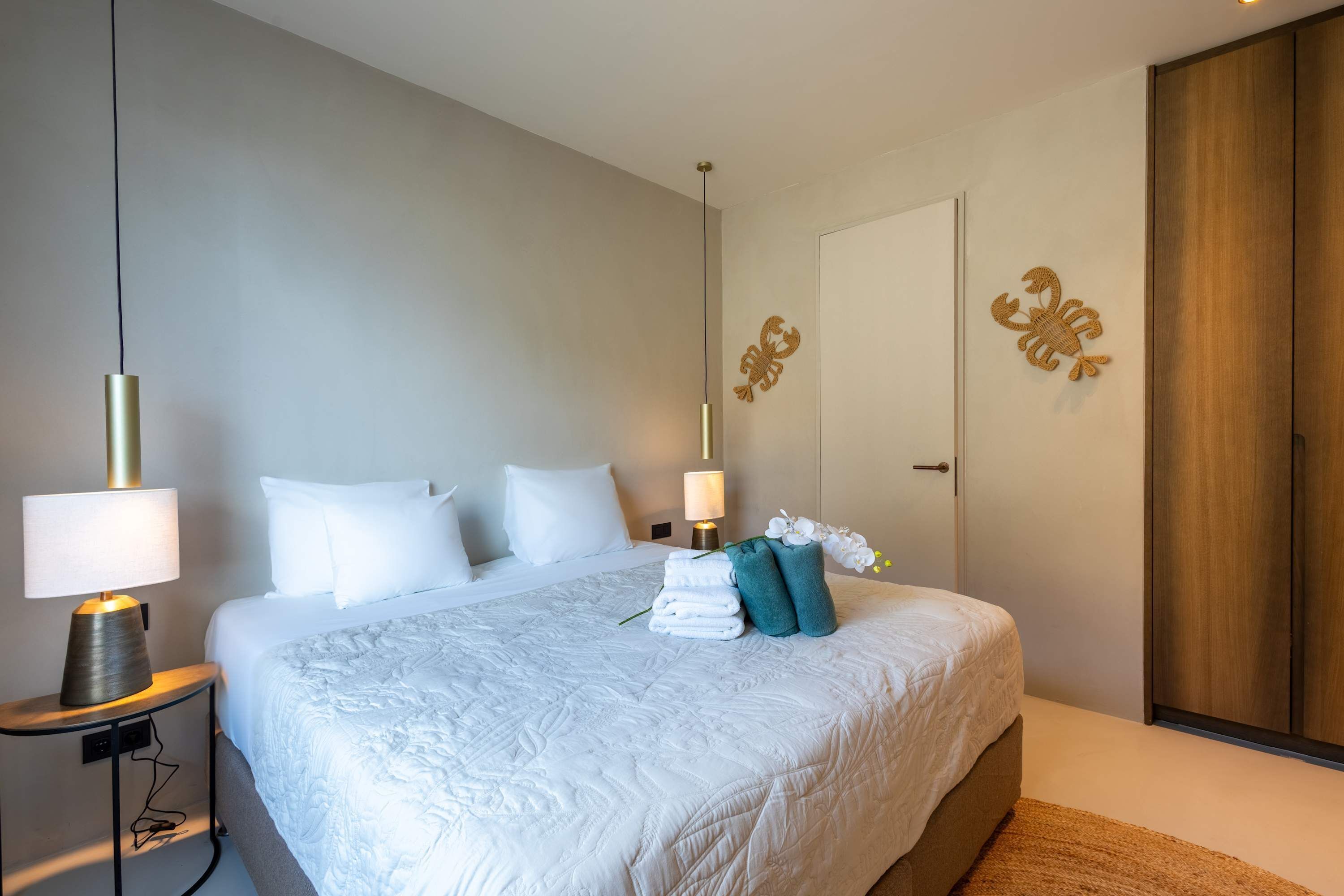 A neatly made bed with white linens, a bedside lamp, and decorative wall art.