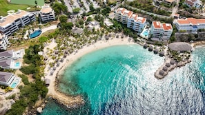 An aerial view of a coastal resort with beachfront properties, a sandy beach, and clear turquoise waters. - The Reef Superior Penthouse With Ocean View (Sint Michiel)
