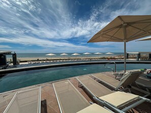 A poolside area with lounge chairs and umbrellas, a beach view, and a clear sky. - Stunning 3rd Floor Beachfront Condo (Puerto Peñasco)