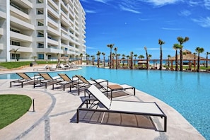 A hotel with a large pool, sun loungers, palm trees, and a clear blue sky. - Stunning 3rd Floor Beachfront Condo (Puerto Peñasco)