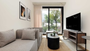 A modern living room with a sofa, coffee table, TV, and a view of a balcony with trees. - w Dreamlike 1BR in the Heart of San Rafael (Mexico City)