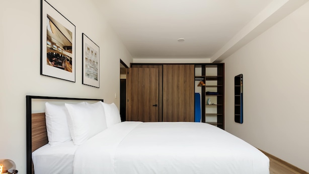 A neatly made bed with white bedding, a bedside table with a lamp, and a wardrobe with a mirror. - w Dreamlike 1BR in the Heart of San Rafael (Mexico City)