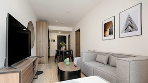 A modern living room with a flat-screen TV, grey sofa, and a coffee table. There are framed pictures on the wall and a dining area in the background. - w Dreamlike 1BR in the Heart of San Rafael (Mexico City)