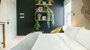 A bedroom with a bed, a bedside table, a chair, a wall-mounted shelf with plants, and a window with blinds. - w Flawless Loft in the Heart of Bocagrande (Cartagena)