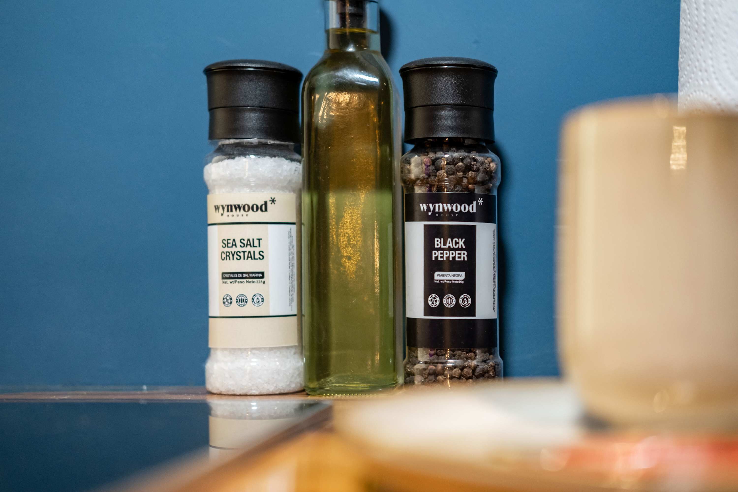 Three bottles of sea salt crystals, black pepper, and a bottle of oil on a shelf.