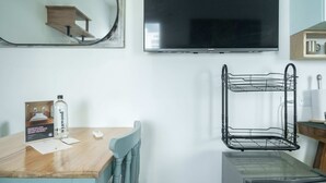 A hotel room with a wooden dining table, a mirror, a flat-screen TV, a black wire shelf, and a poster on the wall. - w Pleasant Loft in the Heart of Bocagrande (Cartagena)