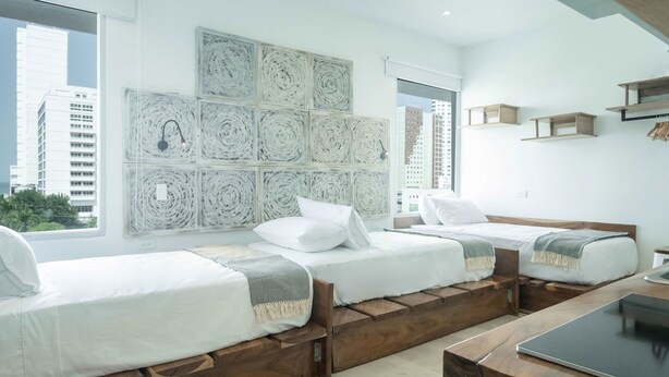 A modern hotel room with two wooden beds, a large window with a city view, and a wall decorated with circular patterns. - w Pleasant Loft in the Heart of Bocagrande (Cartagena)