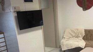 A room with a bed, a television mounted on a cabinet, a door, and a wall decoration. - Athens Cozy Nest - Prime Central Location (Athens)